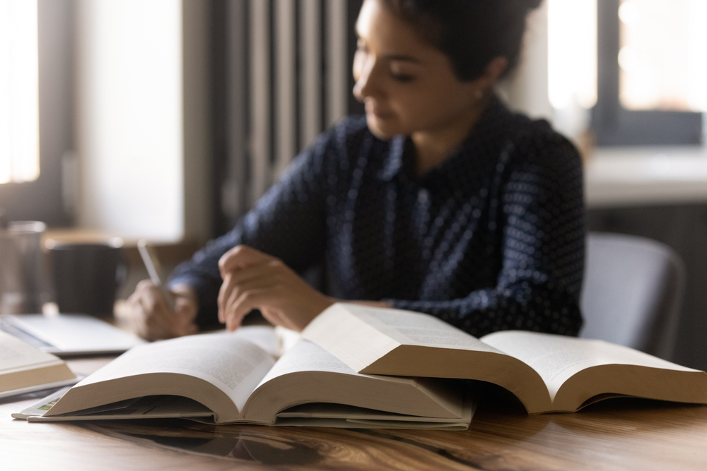 Woman writing with open books in the foreground